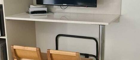 A modern room with a flat-screen TV mounted on a white wall, two wooden chairs, and a metal-framed desk.