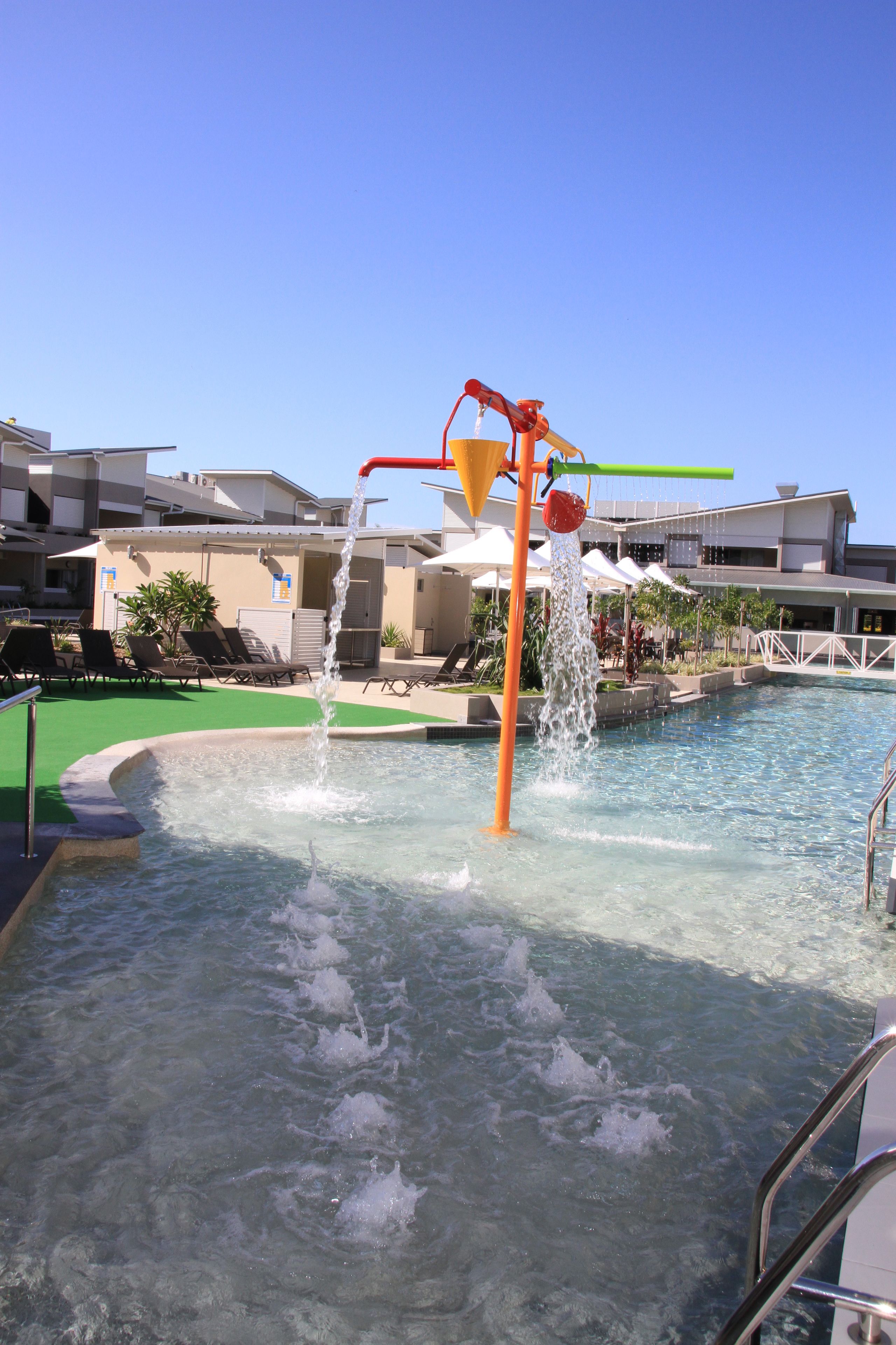 A pool area with a water feature, lounge chairs, and a building in the background.