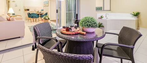 A modern living room with a glass door leading to a kitchen, a round table with chairs, a sofa, and a potted plant.