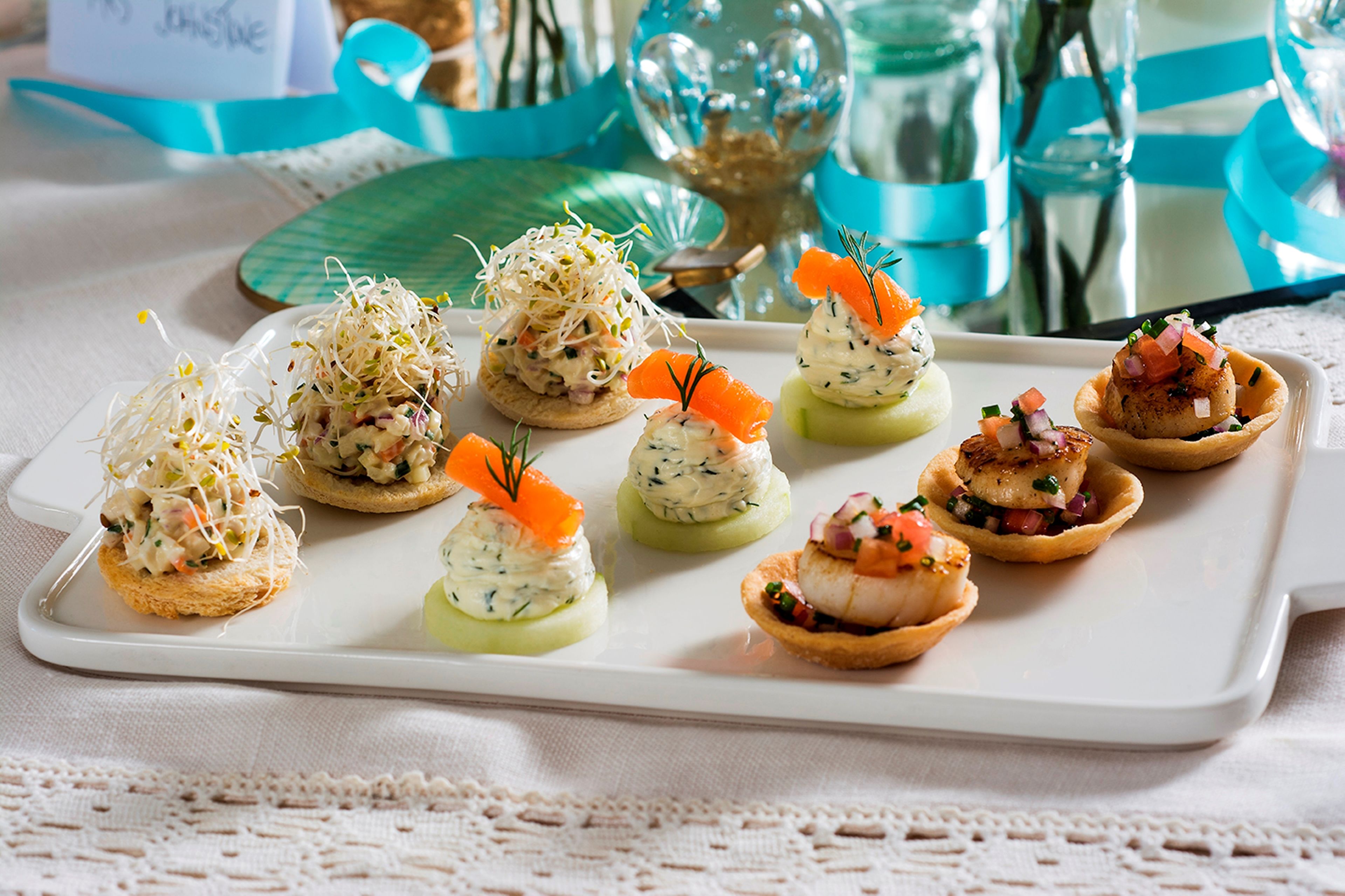 A white rectangular plate with various appetizers, including a salad with sprouts, a fish tartare, and a tart with a topping.