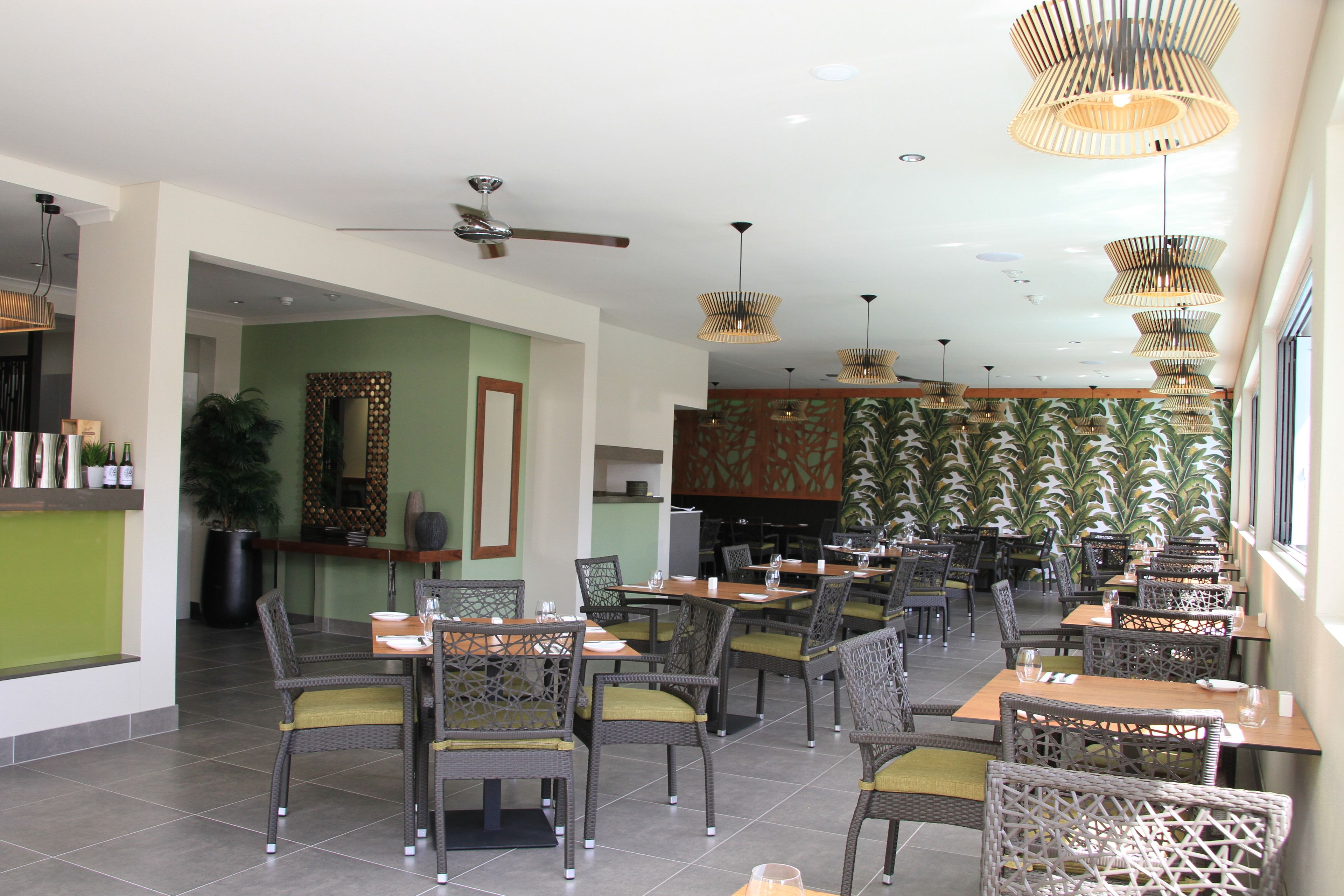 Un restaurant avec des chaises en osier, des tables en bois et des lampes suspendues.