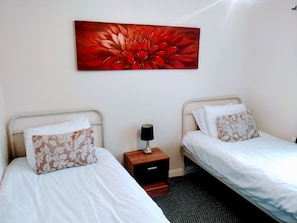 Et hotelværelse med to senge, et natbord med en lampe og et stort blomsterbillede på væggen.
