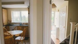 A kitchen with wooden cabinets, a dining table with chairs, and a window with blinds. - Millie and Charley's Apartments (Londonderry)