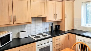 A kitchen with wooden cabinets, a black countertop, a microwave, a toaster, a stove, and a washing machine. - Millie and Charley's Apartments (Londonderry)