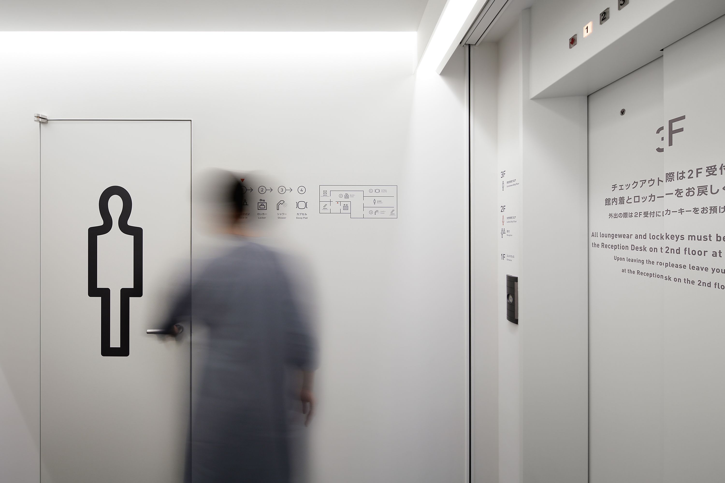 Un intérieur d’hôtel moderne avec un comptoir d’accueil au deuxième étage, une signalétique claire et un design minimaliste.