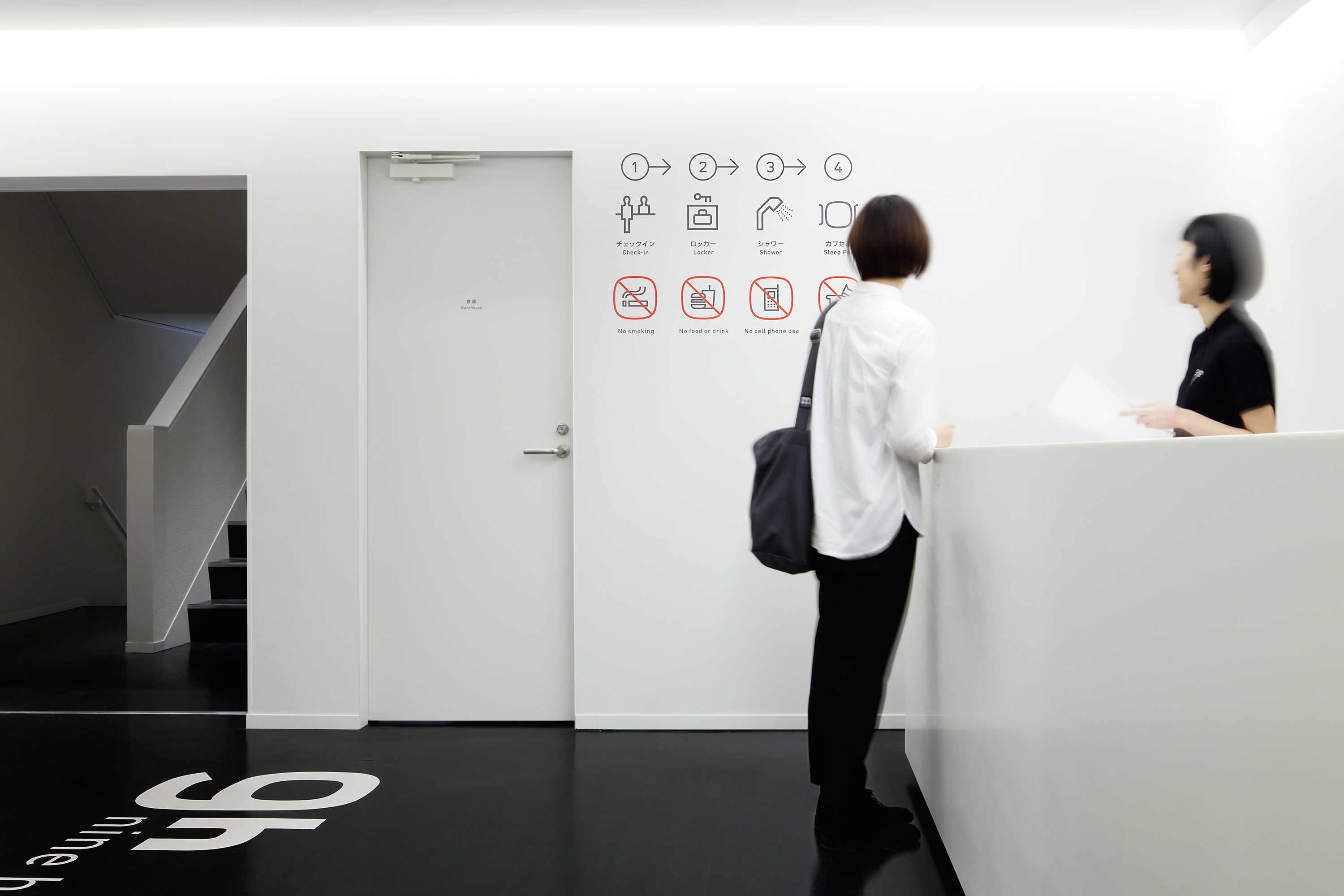 A modern interior with a staircase, a reception desk, and directional signs with icons indicating no smoking, no food or drink, and no cell phone use.