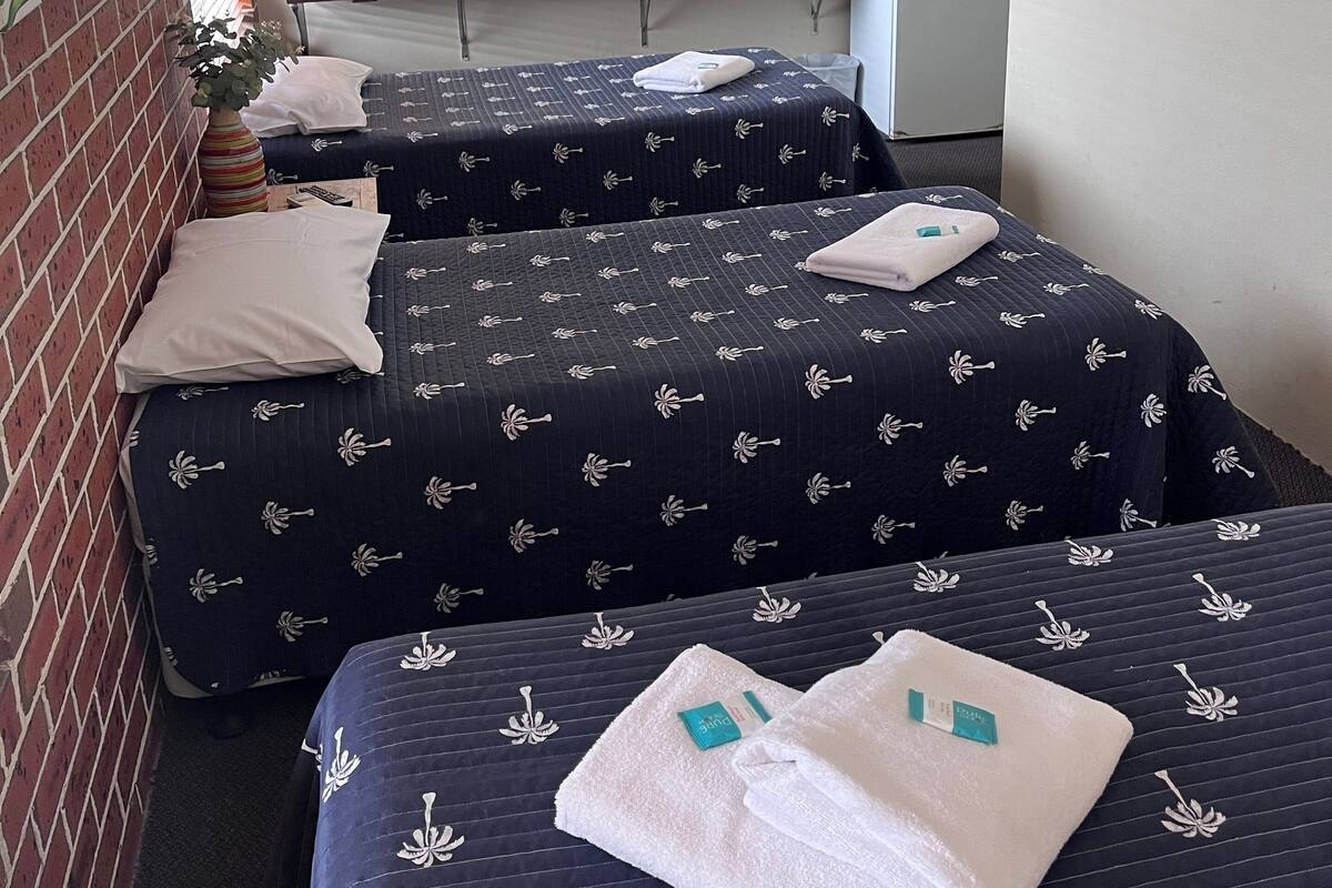 Une chambre d’hôtel avec deux lits, un bureau, un petit coin cuisine et un ventilateur de plafond.