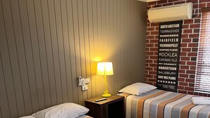 Een hotelkamer met twee bedden, een wandairconditioner, een plafondventilator en een bord met daarop bezienswaardigheden in de buurt.