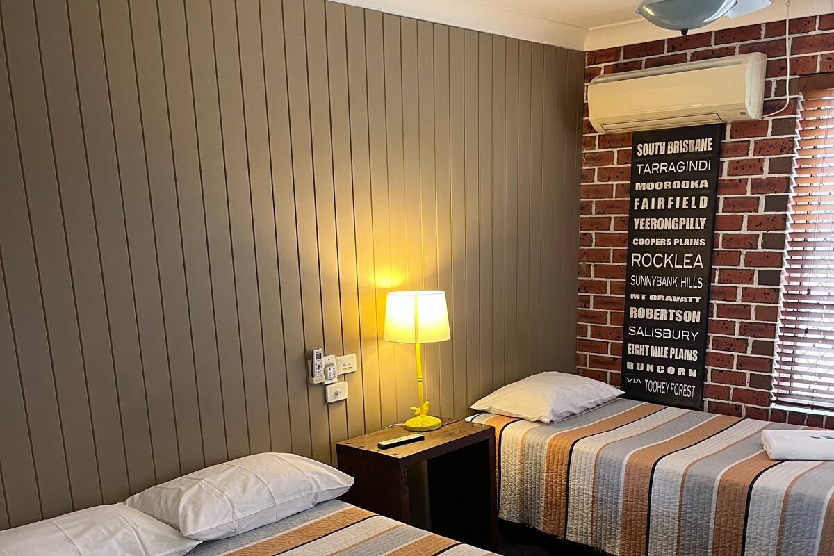 Une chambre d’hôtel avec deux lits, un climatiseur fixé au mur, un ventilateur de plafond et un panneau indiquant les attractions situées à proximité.