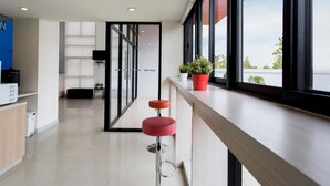 A modern hotel lobby with a reception desk, a bar area with stools, and large windows offering a view of the sky and buildings. - Hop Inn Phitsanulok (Phitsanulok)