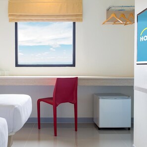 A hotel room with a bed, a red chair, a small refrigerator, a window with a view, and a wooden hanger rack. - Hop Inn Phitsanulok (Phitsanulok)