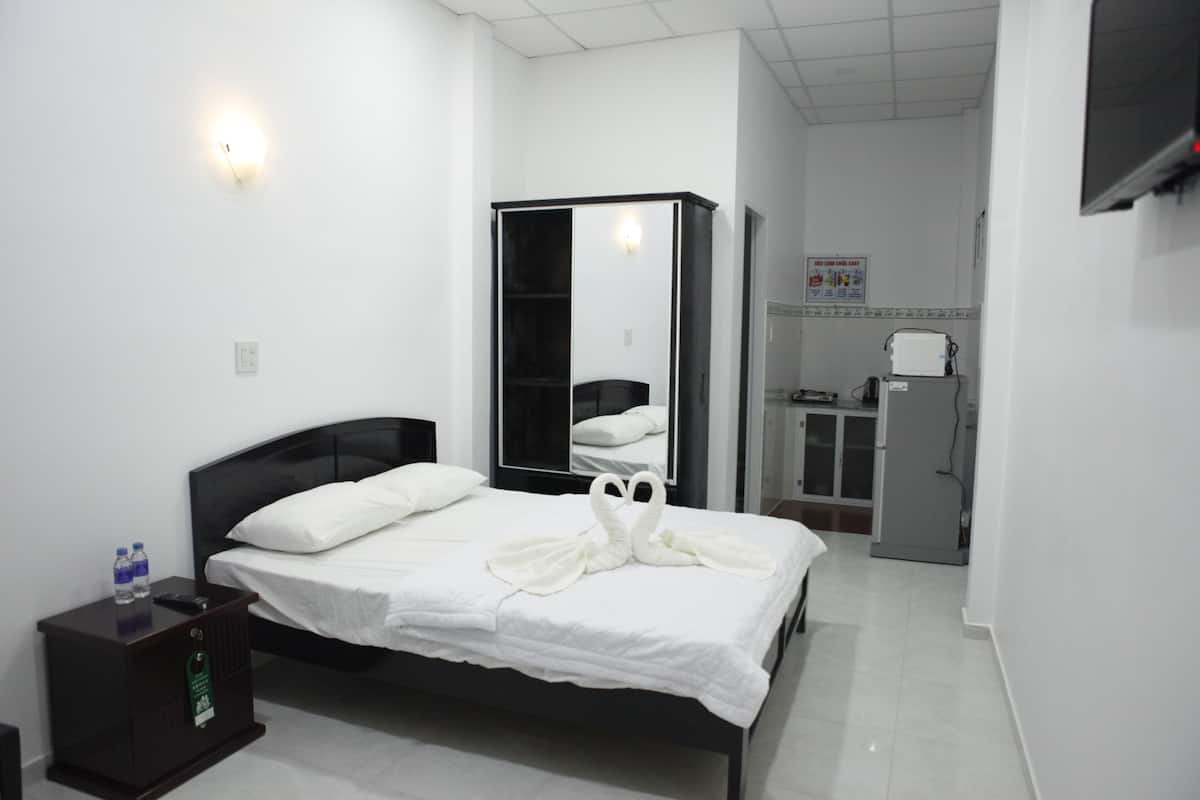 A hotel room with a bed, a wardrobe, a nightstand, a mirror, a refrigerator, and a wall-mounted TV.