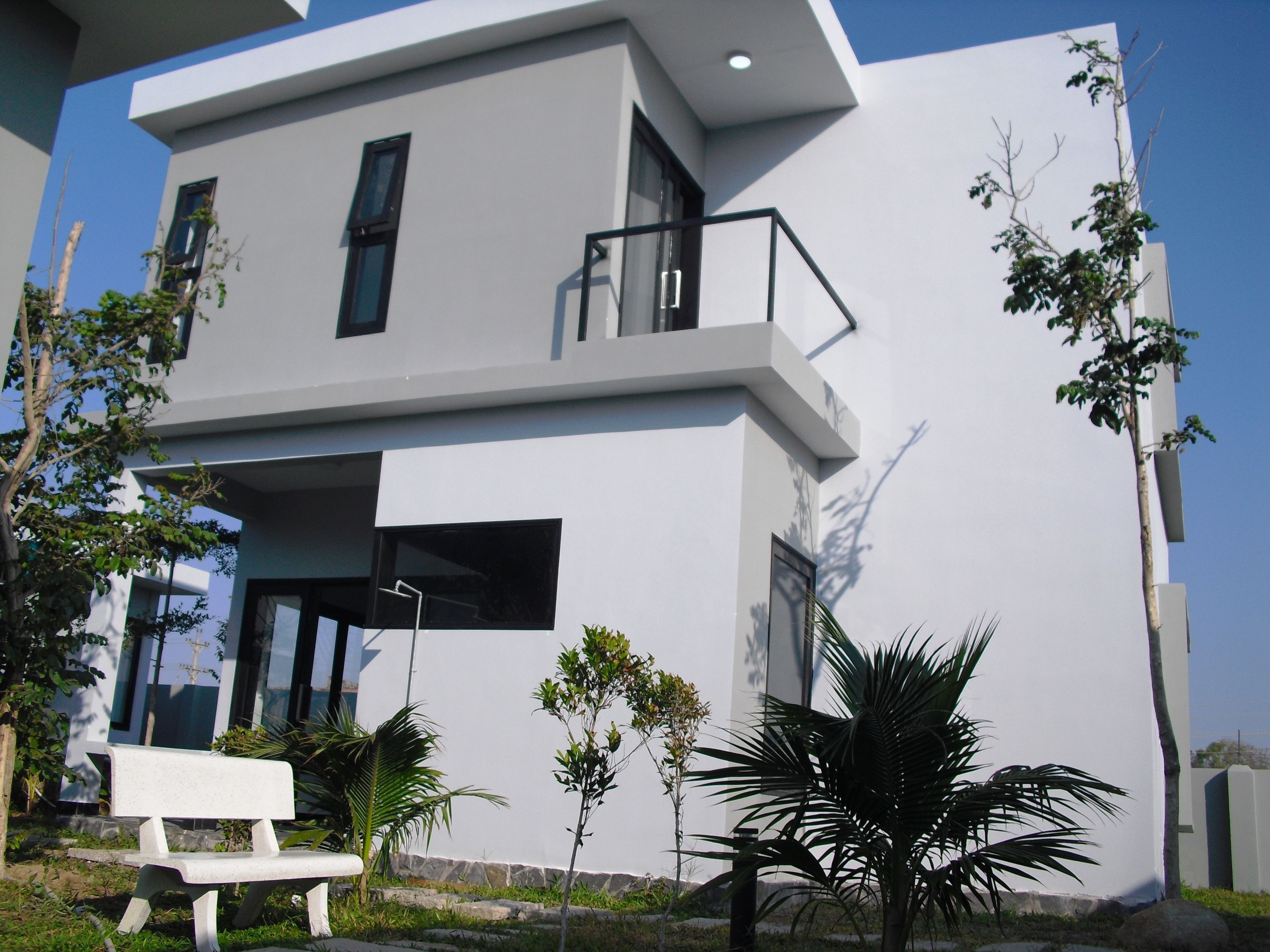 A modern two-story building with a balcony, a bench, and small trees in the foreground.