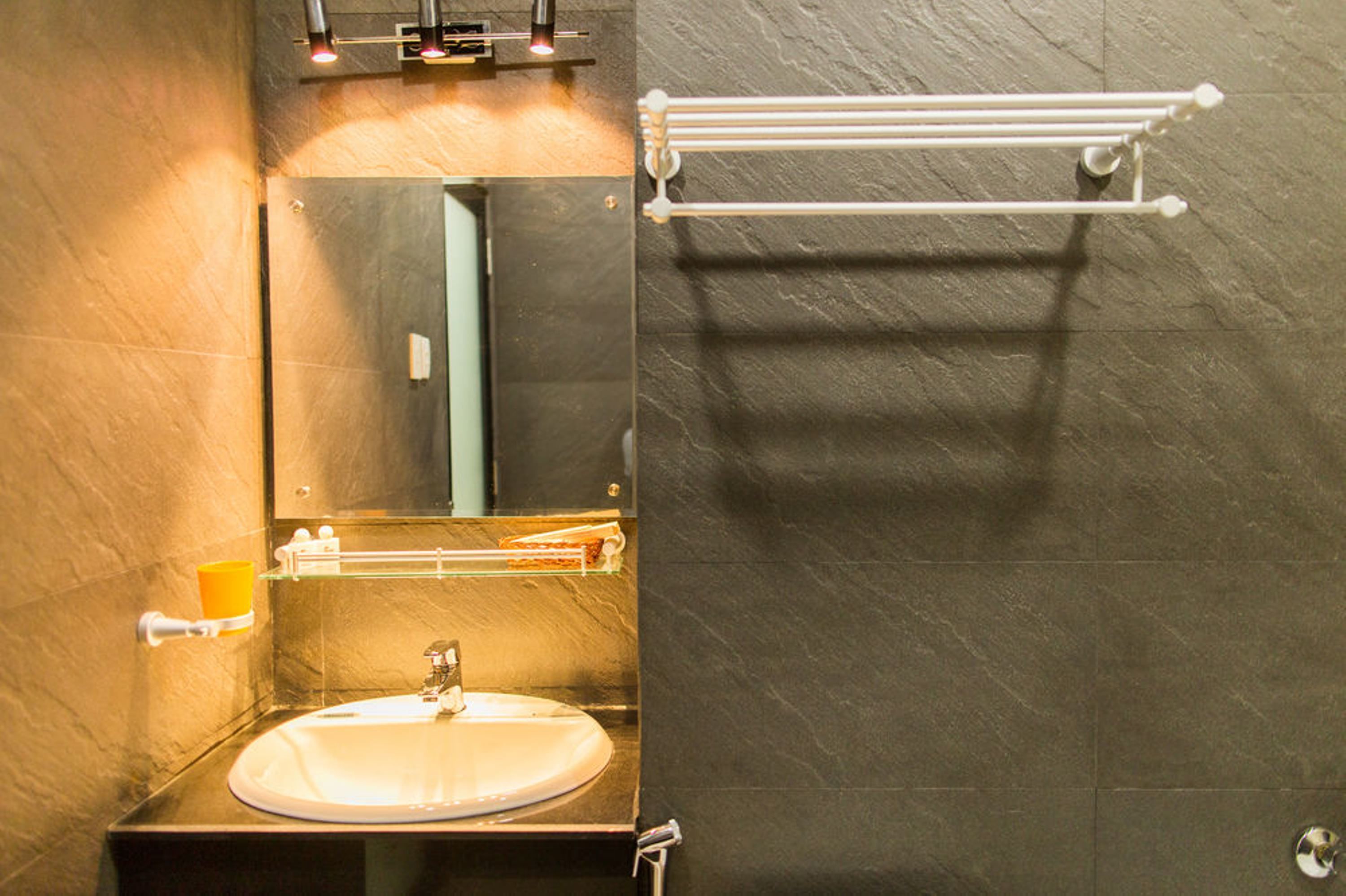 A bathroom with a sink, mirror, towel rack, and a soap dispenser.