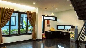 A modern kitchen with a black countertop, a microwave, and a refrigerator. There is a window with curtains and a view of greenery outside. - Van Nguyen Minihouse (Mui Ne)