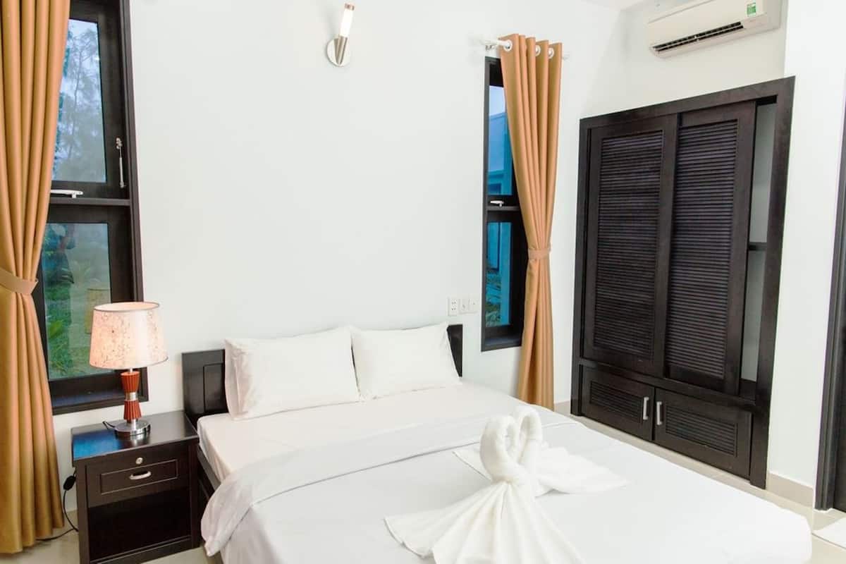 A hotel room with a bed, a nightstand with a lamp, a wardrobe, and a window with curtains.