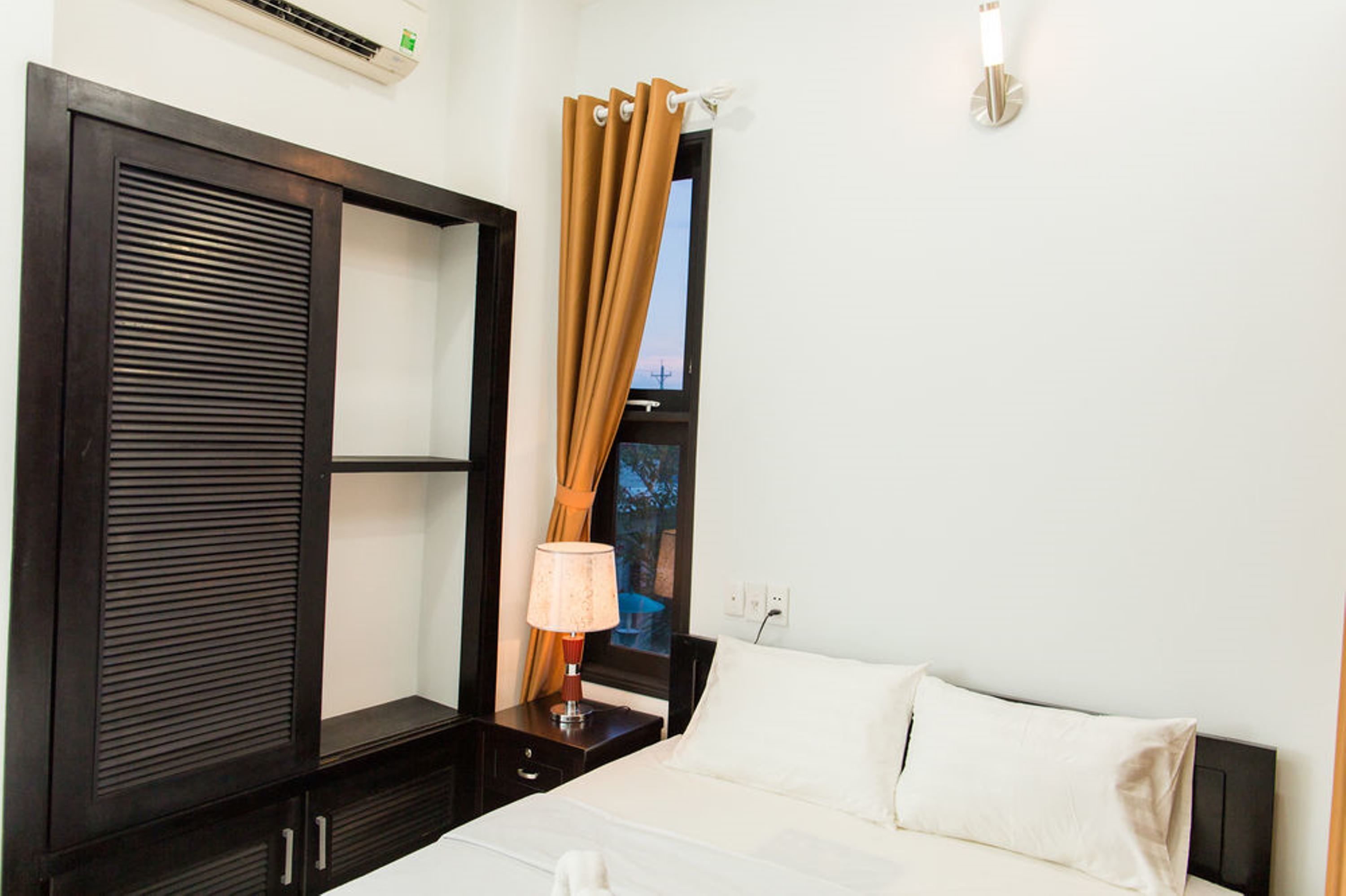 A hotel room with a bed, a nightstand, a lamp, a wardrobe, and a window with curtains.