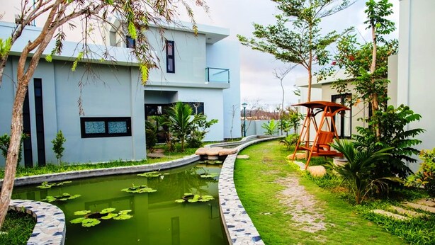 A modern building with a swimming pool surrounded by a stone border, a wooden swing set, and lush greenery. - Van Nguyen Minihouse (Mui Ne)