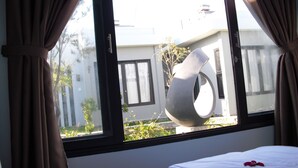 A hotel room with a bed, a large window, and a view of a building outside. - Van Nguyen Minihouse (Mui Ne)