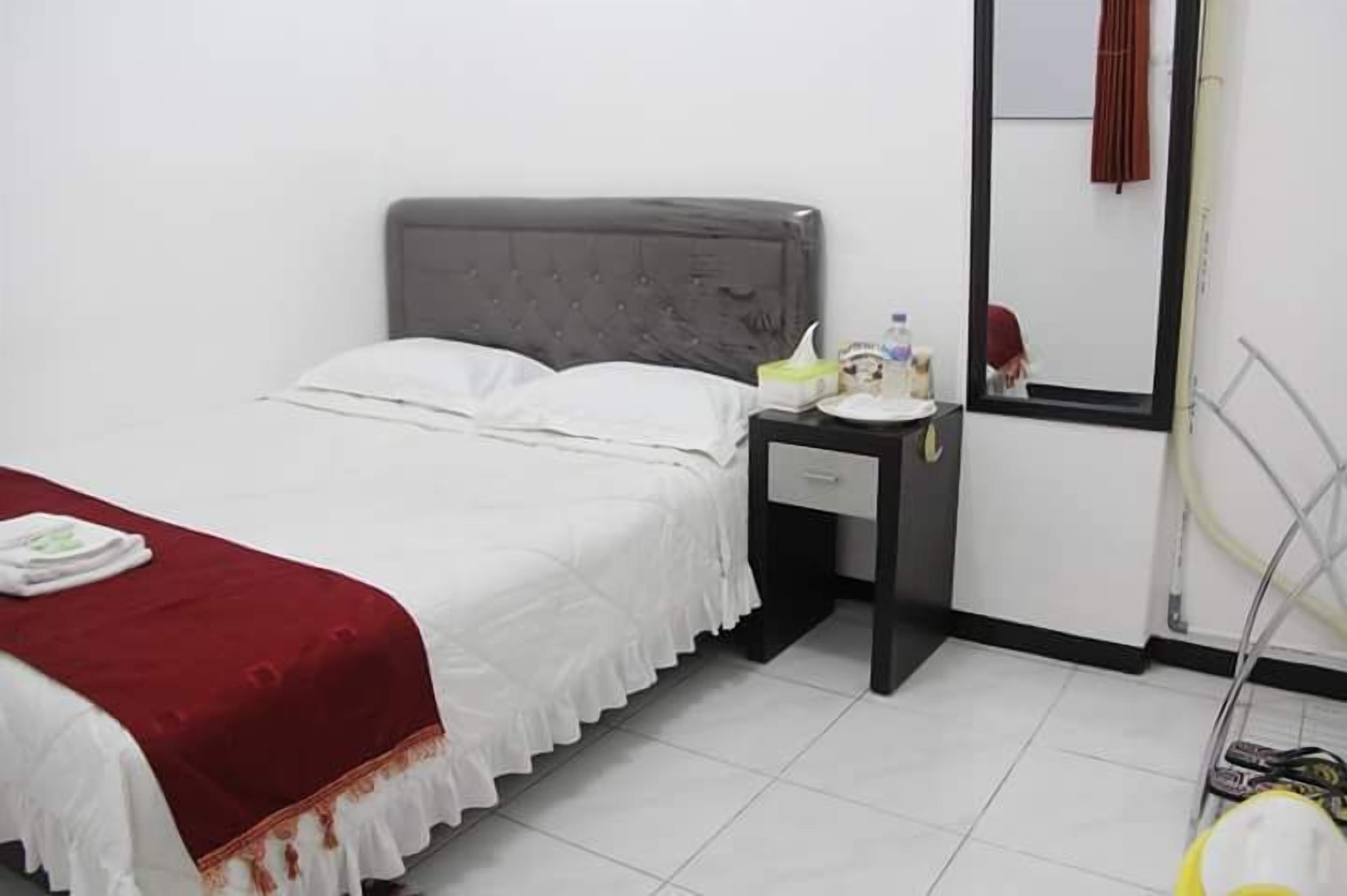 Ein Hotelzimmer mit Bett, Nachttisch mit Lampe und Spiegel an der Wand.
