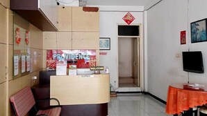A reception area with a reception desk, a bench, a table with chairs, and a television. - Providence Homestay (Surabaya)