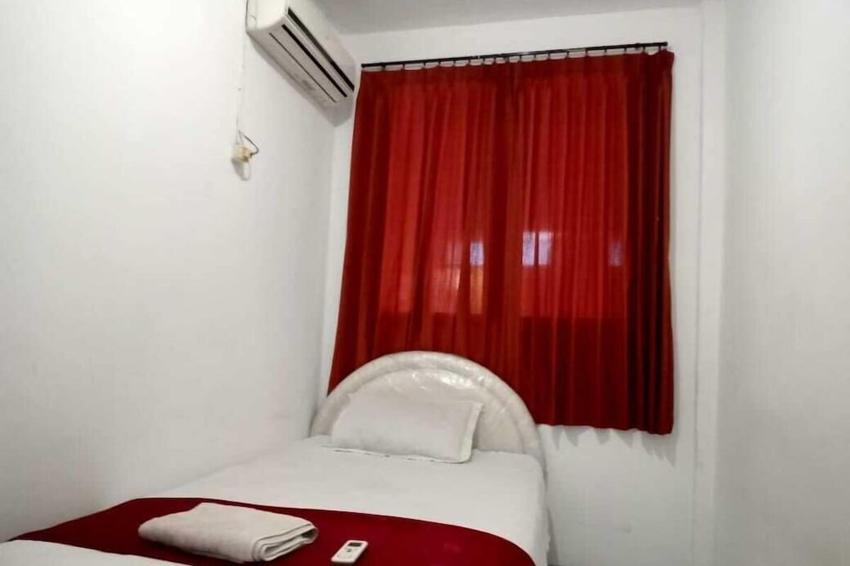 Una habitación con cama, cabecera blanca, cortina roja y pared blanca.