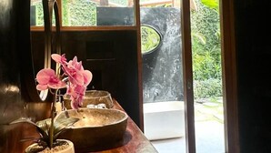 A room with a wooden counter, a potted orchid, and a large window with a view of greenery. - The Apartment Umalas (Keroboken Kelod)