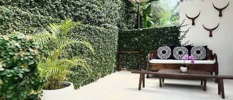 A patio area with a wooden bench, a potted plant, and a wall covered in greenery.