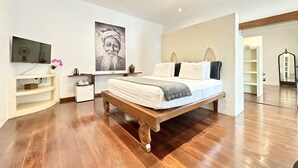 A bedroom with a wooden bed, a TV, a desk, and a large poster on the wall. - The Apartment Umalas (Keroboken Kelod)