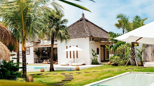 A swimming pool with a thatched-roof building in the background, surrounded by palm trees and a well-maintained lawn. - The Apartment Umalas (Keroboken Kelod)