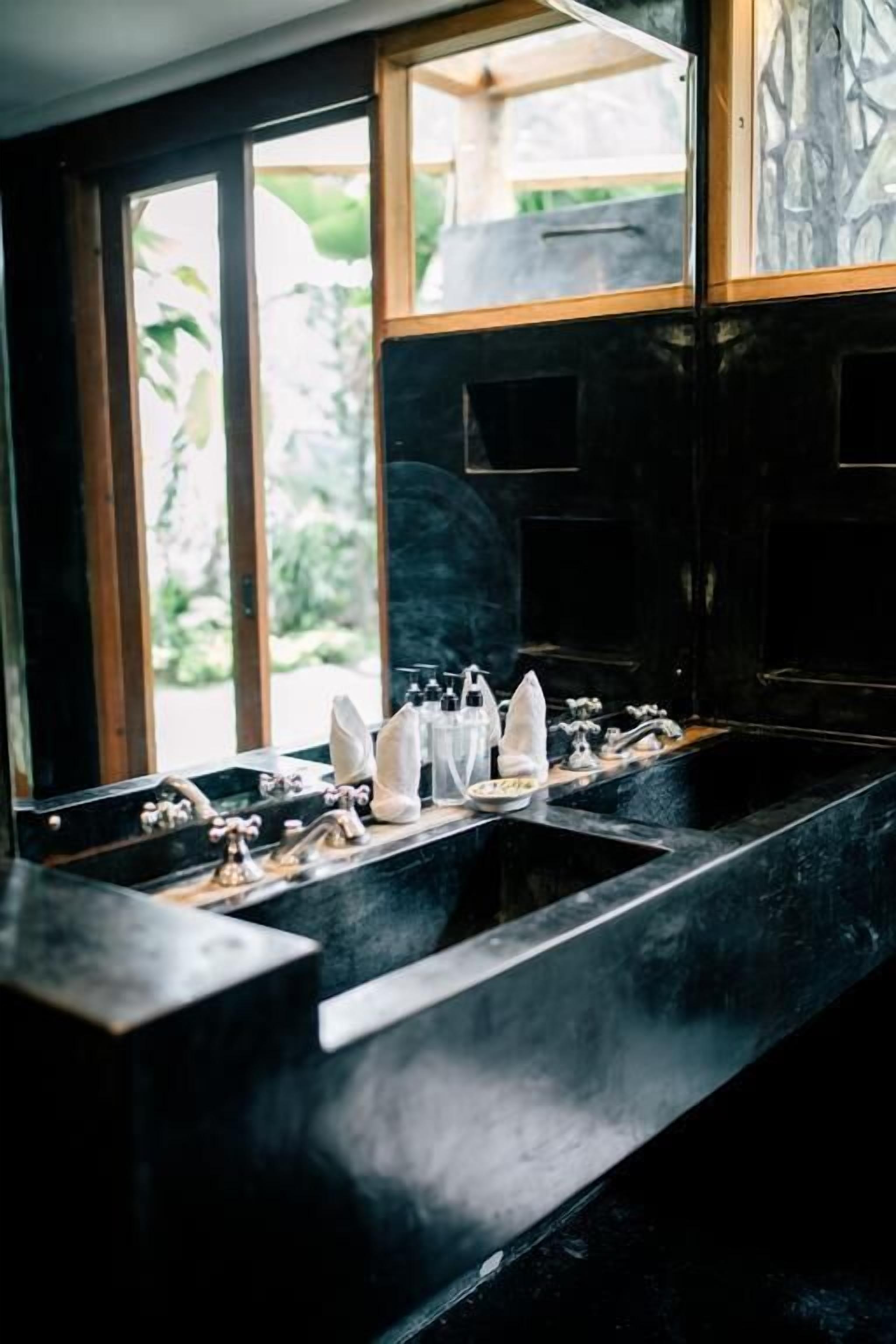 A black marble sink with two faucets, a soap dispenser, and a bottle of hand soap.