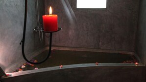 A bathtub with a lit candle, a window, and rose petals scattered on the floor. - Sinharaja Forest Edge (Deniyaya)