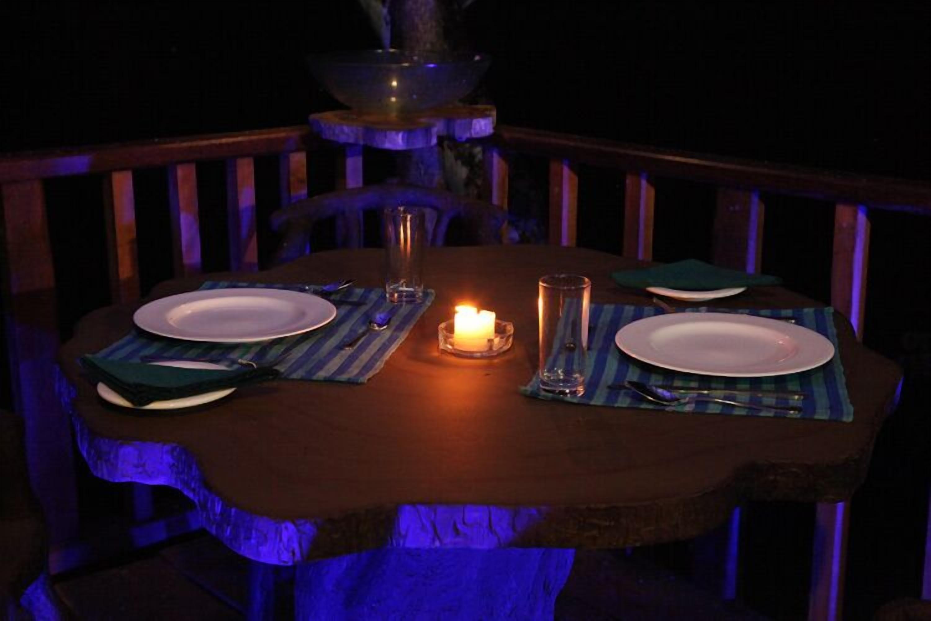 A dining table set with plates, cutlery, and a candle, surrounded by chairs with striped placemats.