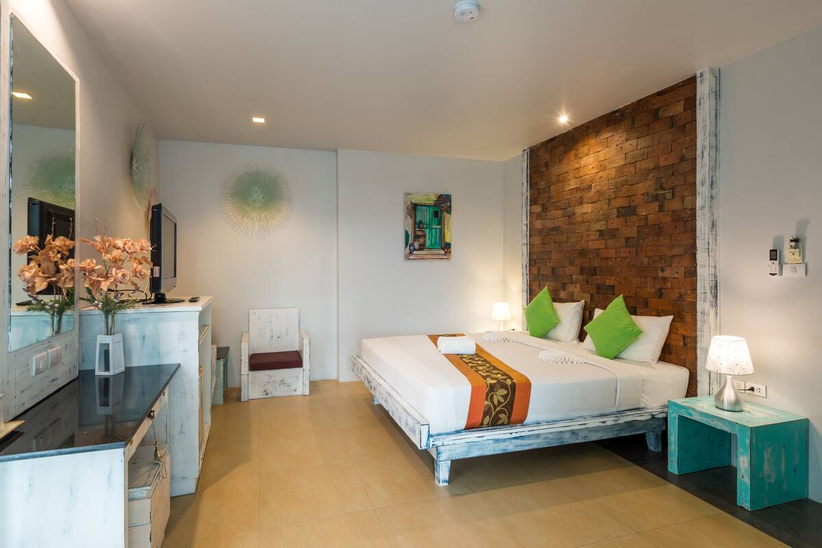Een slaapkamer met een groot bed, een dressoir, een spiegel en een accentmuur van baksteen.