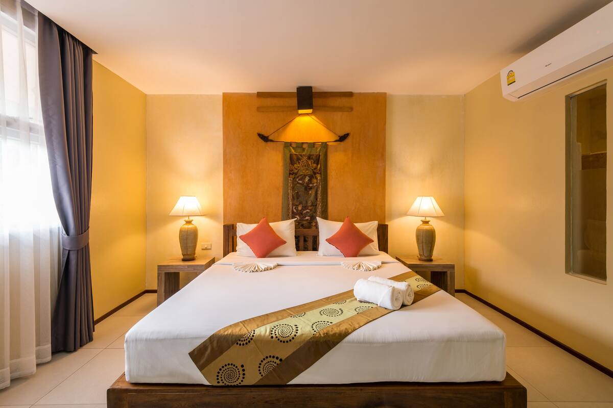 Een hotelkamer met een groot bed, twee bedlampen, een wandairconditioner en een raam met gordijnen.