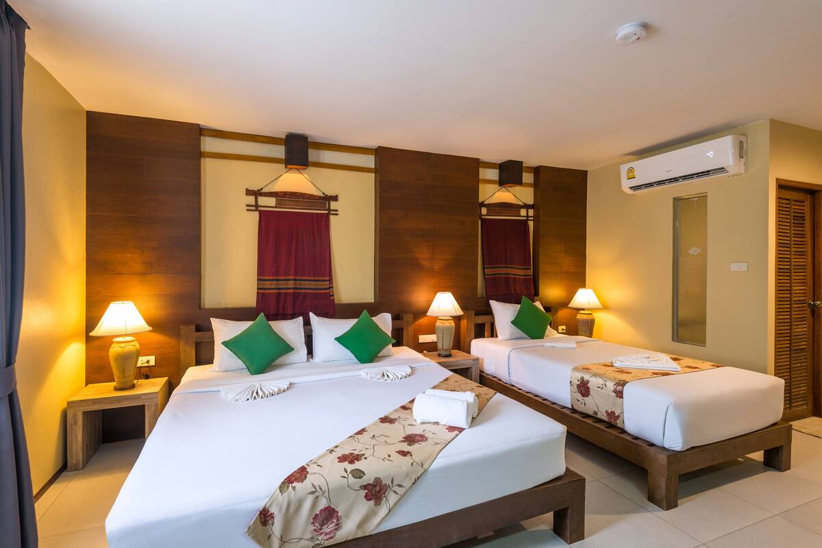 Een hotelkamer met twee bedden, elk voorzien van een nachtkastje, lampen en decoratieve kussens.
