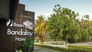 Naamplaatje voor Hotel Baan Bandalay met een logo, omringd door weelderige begroeiing en palmbomen.