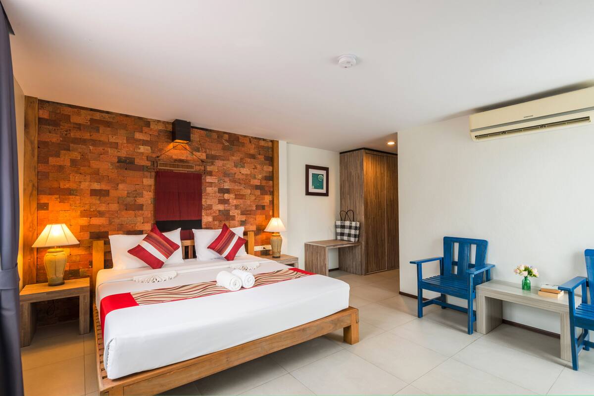Hotelkamer met een accentmuur van baksteen, een houten bed, twee bedlampjes, een bureau met twee stoelen, en een kleine tafel met een vaas.