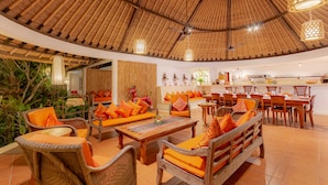 A spacious indoor area with a high thatched ceiling, wicker furniture, and a dining area with wooden tables and chairs. - Bali Akasa Villa (Seminyak)