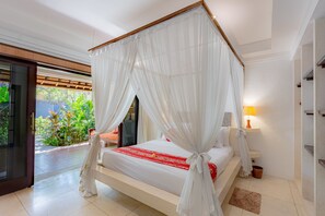 A bedroom with a canopy bed, a bedside table with a lamp, and a view of greenery outside.