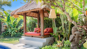 A thatched-roof gazebo with red cushions, a stone pool, and lush tropical plants. - Bali Akasa Villa (Seminyak)