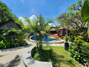 A pool area with lounge chairs, a small hut, and lush greenery.