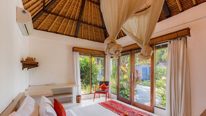 A bedroom with a large bed, a red chair, and a view of greenery outside. - Bali Akasa Villa (Seminyak)