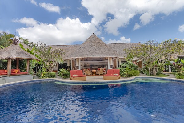 A resort with a swimming pool, red lounge chairs, and thatched-roof structures.