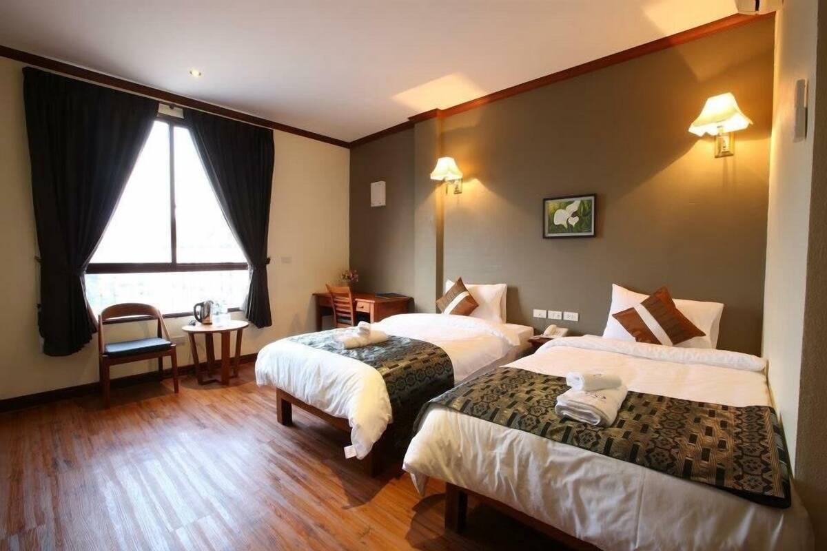 Ett hotellrum med två sängar, ett trägolv, ett skrivbord med en stol och ett fönster med gardiner.