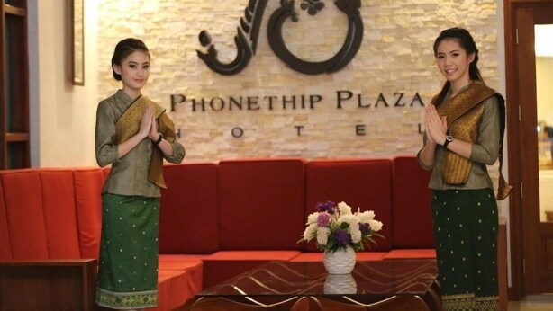 Zwei Personen in traditioneller Kleidung stehen vor einem Empfangsbereich mit einem Schild, auf dem 'PHONETHIP PLAZA HOTEL' steht.