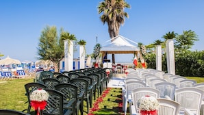 Decoração para cerimônia de casamento ao ar livre, com fileiras de cadeiras, um gazebo e palmeiras.