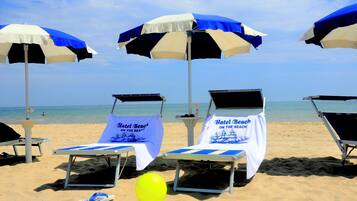 Des chaises de plage avec des parasols et des serviettes, un ballon de plage jaune et une sandale sur le sable.