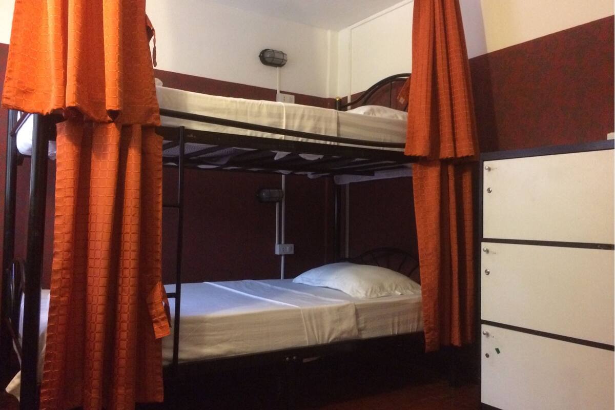 A bunk bed room with orange curtains, a small desk, and a wardrobe.