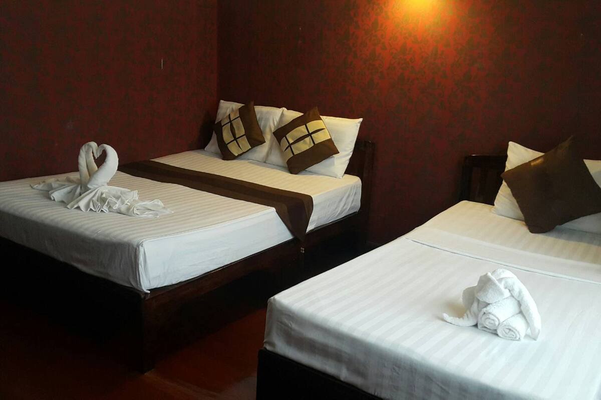 Two single beds with white linens and brown pillows, a wooden headboard, and a red patterned wall.